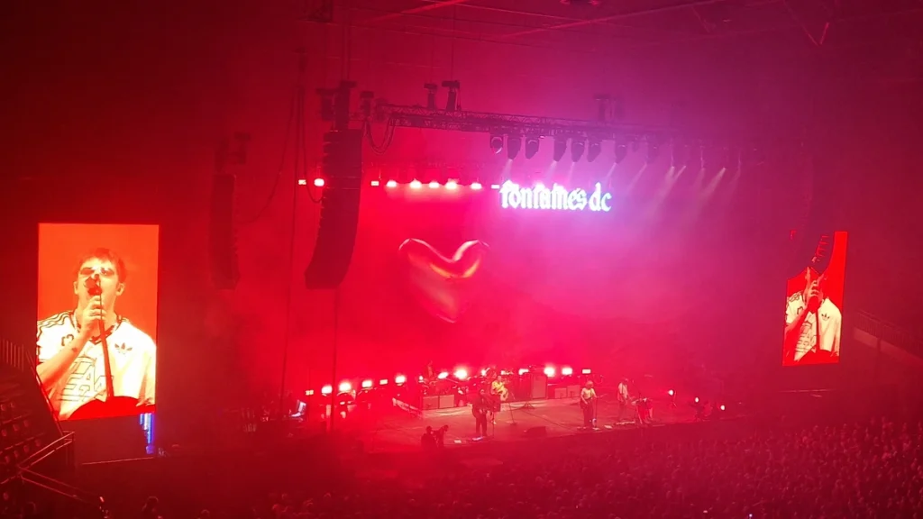 Fontaines D.C. performing in an arena under red lighting with the band's logo behind them