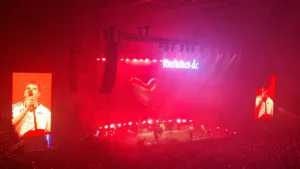 Fontaines D.C. performing in an arena under red lighting with the band's logo behind them