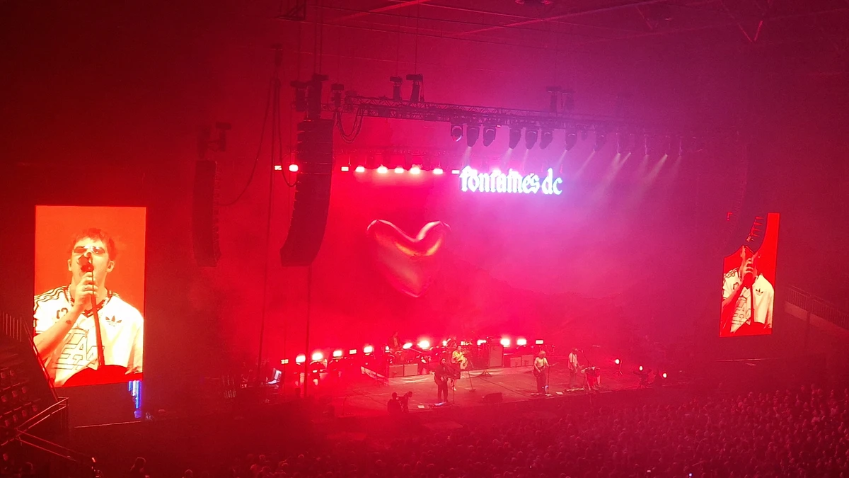 Fontaines D.C. performing in an arena under red lighting with the band's logo behind them