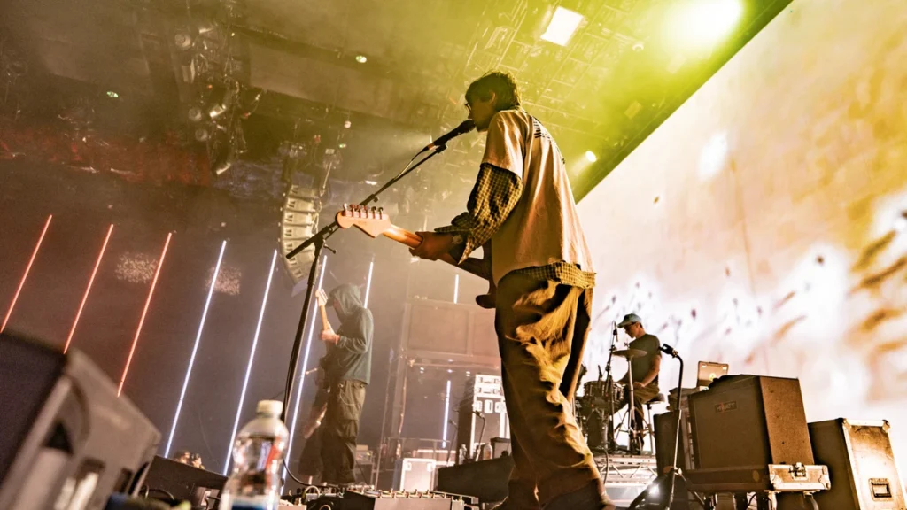 DIIV on stage in front of a large illuminated screen with vertical light bars and haze