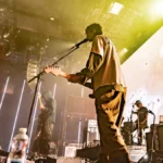 DIIV on stage in front of a large illuminated screen with vertical light bars and haze