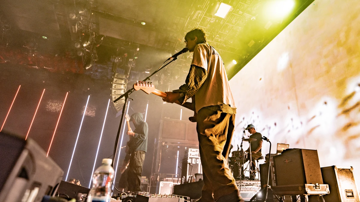 DIIV on stage in front of a large illuminated screen with vertical light bars and haze
