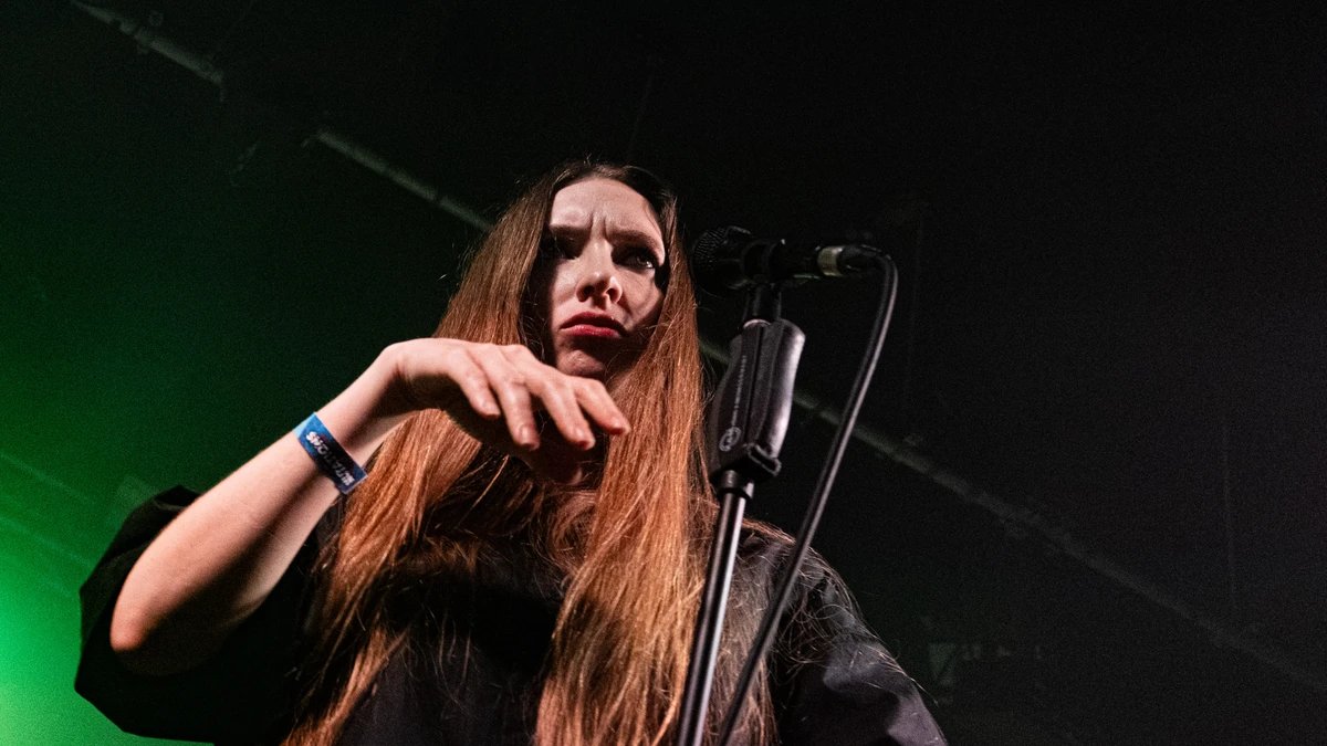 Florence Shaw of Dry Cleaning at the microphone in green stage light